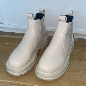 Beige chunky chelsea boots - Säljer ett par beige chunky chelsea boots med kraftig sula och resår på sidorna. Skorna har rund tå och dragflikar både fram och bak för enkel påtagning. Perfekta för att lyfta din outfit med en modern touch.