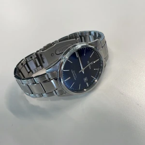 Silverfärgad herrklocka från Festina med ljus blå urtavla - Stilren klocka från Festina med blå urtavla, datumvisning och silverfärgat armband i metall. Klassisk design med tydliga index och kvartsverk. Perfekt accessoar för dig som gillar en tidlös look.