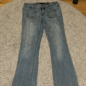 Ljusblå bootcut jeans med fickor fram och bak - Säljer ett par ljusblå jeans med bootcut passform. Jeansen har stora fickor med knappar både fram och bak. De ser ljusare ut i verkligheten än på bilden! Köpt för runt 900kr, säljer då det stod fel mått på jeansen där jag köpte de från💗 skulle säga att de kanske är i storlek L eller M? Midjemått: 38 innerben: 74💕