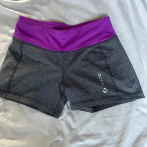 Grå träningsshorts med lila midja från SOC - Snygga grå träningsshorts från SOC med bred lila midja. Perfekta för gymmet eller löpning, med bekväm passform och stretchigt material. Logga på benet och elastisk midja för extra komfort.Skriv privat för fler bilder eller andra frågor 💞