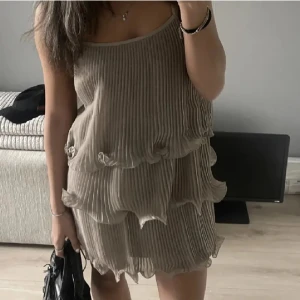 volangklänning - Säljer en beige kortklänning med volanger. Klänningen är använd 1 gång och är i mycket bra skick.