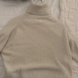 Beige ribbad polotröja - Säljer en beige ribbad polotröja med lång ärm. Tröjan är stickad och har en hög polokrage som ger en mysig känsla. Perfekt för kyligare dagar och enkel att matcha med olika outfits.