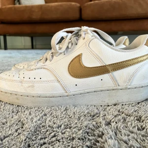 Nike sneakers i vitt och guld - Säljer ett par klassiska Nike sneakers som liknar air force 1  med guldiga detaljer och swoosh. 