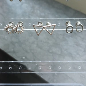 Set med tre par silvriga örhängen. Säljer alla :) - Säljer ett set med tre par silvriga örhängen i olika former: solformade, trekantiga och runda. Alla är små och stilrena, perfekta för att mixa och matcha. Kommer i en röd organzapåse.