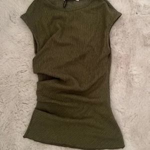 Olivgrön ribbad topp från Pull&Bear - Säljer en olivgrön ribbad topp från Pull&Bear. Toppen har en tight passform, är ärmlös och har en enkel, stilren design. Perfekt för dig som gillar minimalistisk stil och mjuka material.