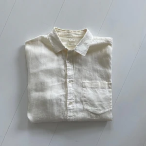 Vit linneskjorta med bröstficka - Klassisk vit skjorta i linne från Arket med lång ärm och bröstficka. Skjortan har knappar framtill och en avslappnad passform, perfekt för varma dagar. Enkel och stilren design med mjukt material.