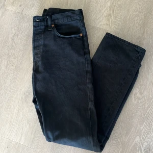 Svarta Levi's 501 jeansbyxor - Säljer ett par klassiska svarta Levi's 501 jeans med raka ben och femficksmodell. Byxorna har knappgylf och är tillverkade i kraftigt denimtyg. Perfekta för dig som gillar tidlös stil och premiumkänsla.