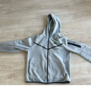 Grå hoodiejacka från Nike - Grå nike tech till salu. Säljer denna Nike tech, i mycket gott skick. Ända defekt är en skråma, men inget som påverkar looken. Självklart äkta, har befräktelse från Unisport! Nypris just nu är ~1299 kr. Mitt pris 499 kr.