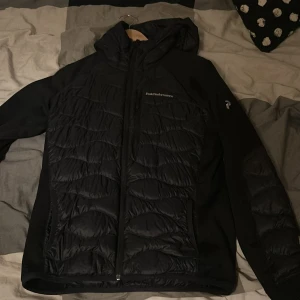 Svart pufferjacka från Peak Performance - Säljer en svart pufferjacka från Peak Performance med huva och dragkedja. Jackan har quiltad framsida och är tillverkad i syntetmaterial. Perfekt för kyliga dagar och har en sportig look.