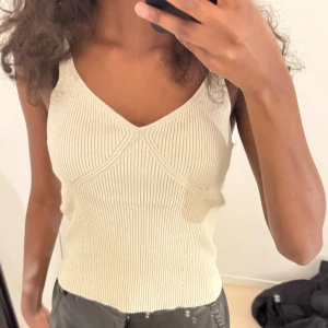 Ribbad vit linnetopp - Säljer en ribbad vit linnetopp med smala axelband och v-ringad hals. Toppen har en figurnära passform och är perfekt för varma dagar. Enkel och stilren design som passar till mycket.