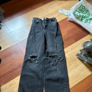 Svarta jeansbyxor med slitningar från g perfect jeans - Säljer ett par svarta jeansbyxor från g perfect jeans i rak modell. Byxorna har tydliga slitningar och hål vid knäna för en trendig look. Klassisk femficksdesign och normal passform. Perfekta för dig som gillar en avslappnad stil.