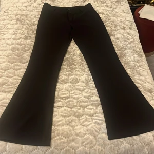 Svarta low bootcut kostymbyxor - Snygga svarta low kostymbyxor med bootcut-passform. Byxorna har klassisk design med fickor bak och stängs med knapp och dragkedja framtill. Perfekta för en stilren look. Kostymbyxorna är små i storleken så den passar i xs och s med. Aldrig använt. 