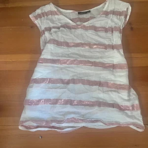 Vit och rosa randig topp från KappAhl - Säljer en jättefin vit topp från KappAhl med glittriga rosa ränder. Toppen har korta ärmar och en rund halsringning. Perfekt för sommaren och enkel att matcha med jeans eller kjol. Jättefint skick för bra pris!