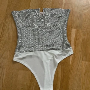 Silverglittrig tubtopp-body - Säljer en snygg tubtopp-body med glittriga paljetter i silver.Toppen är axelbandslös och har en figurnära passform, men tyvärr passade den inte :( 