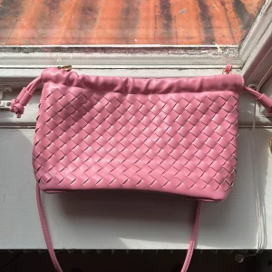 Rosa axelväska från Hunkemöller - Säljer en söt rosa axelväska från Hunkemöller med flätad design och med axelrem. Väskan har dragsko upptill och guldfärgade metalldetaljer. Jättefin och är i nyskick då den inte använt alls. Priset går alltid att diskutera😊