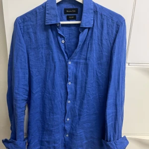 Blå linneskjorta från Massimo Dutti - Snygg blå skjorta i 100% linne från Massimo Dutti. Skjortan har klassisk krage, långa ärmar och knäppning framtill. Perfekt för en stilren och avslappnad look.