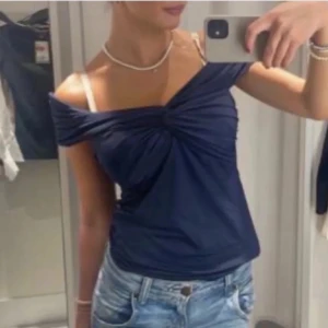 Mörkblå offshoulder topp - Säljer en mörkblå offshoulder topp med twistad detalj framtill. Toppens material är mjukt och stretchigt, perfekt för en trendig look. Passar snyggt till jeans eller kjol.