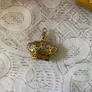 Guldfärgat kronhänge med färgade stenar - Säljer ett guldfärgat hänge i form av en krona, dekorerad med små färgade stenar i rött, blått och grönt. Perfekt som detalj till halsband eller armband. Ger en kunglig touch till din stil. Stor i storlek