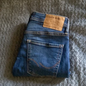 Blå jeans från Jack & Jones - Säljer ett par klassiska blå jeans från Jack & Jones med fem fickor och snygga kontrastsömmar. Skick 10/10 använda några fåtal gånger. Slim fit. 27/30. Nypris 900kr