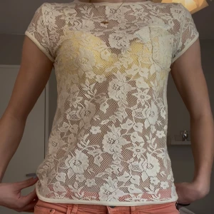 Vit blommig spetsblus - Säljer en vit blommig spetsblus med korta ärmar och rund hals. Blusen är genomskinlig. Står inget varumärke. 