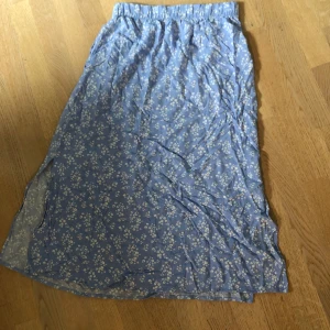 Blå blommig långkjol  - Säljer en ljusblå långkjol från lager 157 med vitt blommigt mönster. Kjolen har resår i midjan och är gjord i ett lätt och mjukt material, perfekt för varmare dagar. Supersöt och enkel att matcha med olika toppar!