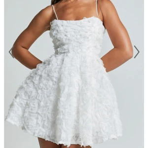 Vit kortklänning med 3D-blommor och tunna axelband - Superfin vit kortklänning med tunna axelband och 3D-blommor över hela tyget. Klänningen har en utsvängd kjol och romantisk känsla, perfekt för speciella tillfällen. Materialet är lätt och ger en fluffig look. Klänningen är i storlek 36 säljer då den är för liten för mig. Prislapp sitter kvar på, klänningen är från showpo. Nypris ca 1100kr
