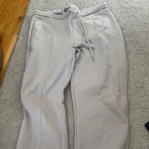 Beige mjukisbyxor med snörning från 157 - Säljer ett par beige mjukisbyxor från 157 med raka ben och snörning i midjan. Byxorna har en enkel och stilren design med söm längs benen. Perfekta för en avslappnad stil.