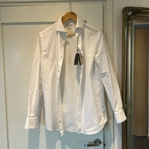 Vit skjorta från Massimo Dutti - Klassisk vit skjorta från Massimo Dutti med lång ärm och knappar framtill. Tillverkad i lättskött italienskt tyg. Perfekt för en stilren och tidlös look.