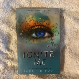 Ignite Me - Boken 'Ignite Me' av Tahereh Mafi har ett omslag med ett konstnärligt öga omgivet av färgstarka detaljer och blommor. Framsidan har texten 'Fear will learn to fear me'. Baksidan innehåller en kort beskrivning av handlingen och små bilder på andra böcker i serien. Tredje boken i serien. 