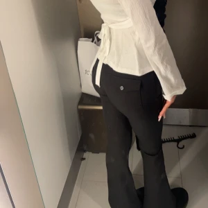 Svarta kostymbyxor från Gina Tricot - Säljer ett par svarta kostymbyxor från Gina Tricot med fickor bak och knappar framtill. Byxorna har bootcut-modell, vilket ger en snygg och tidlös siluett. Perfekta att styla med både sneakers och klackar.