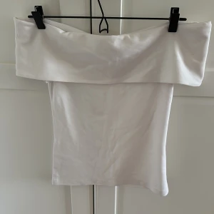 Vit offshoulder tubtopp från COS - Säljer en stilren vit offshoulder tubtopp från COS. Toppen har en bred kant upptill som ger en snygg och modern look. Perfekt att matcha med både jeans och kjol. Materialet känns mjukt och följsamt.