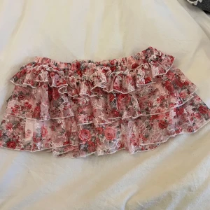 Blommig volangkjol i spets - Supersöt kortkjol med volanger i rosa och vit spets med blommigt mönster. Den har shorts under för säkerhets skull och är jätte söt!!😇