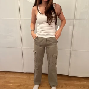 Beiga cargopants med fickor - Säljer ett par beiga cargopants med flera stora fickor på sidorna. Byxorna har en rak passform och normal midja. Perfekta för en avslappnad och trendig stil. Man kan även vika ner dom för med lowwaist stil