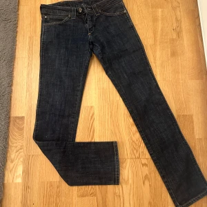 Mörkblå jeansbyxor från Wrangler - Säljer ett par klassiska mörkblå jeans från Wrangler. Byxorna har normal passform och raka ben, med traditionell femficksdesign och knappgylf. Perfekta till vardags för en stilren look.