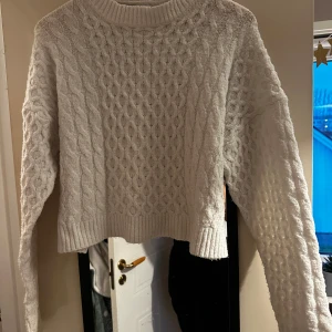 Vit stickad croppad tröja från INSIDE - Säljer en vit stickad tröja från INSIDE i croppad modell. Tröjan har ett fint kabelstickat mönster, rund halsringning och långa ärmar. Perfekt för lager-på-lager och passar till många olika outfits.