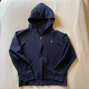 Mörkblå hoodie från Polo Ralph Lauren - Mörkblå hoodie med dragkedja från Polo Ralph Lauren. Modellen är 180 och storlek L, den är 60 cm lång och 55 cm bred, den har inga hål fläckar eller missfärgningar, hör av dig om du har frågor!