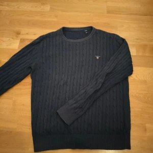 Mörkblå kabelstickad Gant - Säljer en mörkblå kabelstickad tröja från GANT med loggan broderad logga på bröstet. Perfekt för grisch personer eller folk med avslappnad stil. Storlek XS-S. Hör av dig vid funderingar