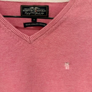 Rosa v-ringad tröja från Hampton Republic - Säljer en rosa v-ringad tröja från Hampton Republic i bomull. Tröjan har långa ärmar, ribbade muddar och en liten broderad logga på bröstet. Perfekt för en stilren och avslappnad look.