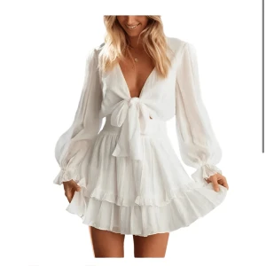 Vit omlottklänning med volang - Säljer en superfin vit kortklänning med långa, transparenta ärmar och volangkantad kjol. Klänningen har omlottknytning framtill och markerad midja med smock. Perfekt för sommarens alla tillfällen! Tex studenten! Aldrig använt, finns ingen prislapp kvar men aldrig aldrig använd.  köpt nyligen denna månad men var tyvärr inte min stil så säljer vidare den, köpte den inte på rea men verkar som de är rea på den nu så den ligger på 399kr. Storleken är som en blandning mellan m/L