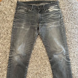 Gråa Levi's 511 jeans - Säljer ett par gråa Levi's 511 jeans med snyggt slitna detaljer och klassiska fem fickor. Jeansen har en rak passform och är i stretchigt denim. Perfekta för dig som gillar en stilren och avslappnad look.