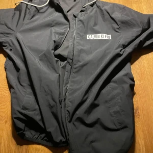 Svart vindjacka från Calvin Klein - Säljer en svart vindjacka från Calvin Klein i storlek S. Perfekt för dig som gillar stilrena och sportiga plagg. Passar perfekt nu till våren/sommaren. Inget fel alls på jackan säljer för den är för liten för mig.