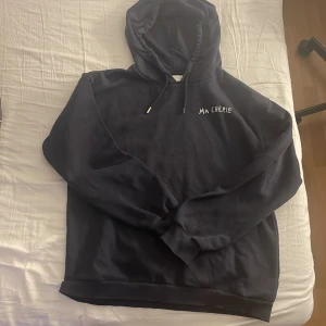 mörkblå hoddie med tryck 'Ma Chérie' - Säljer en mörk blå hoodie med texten 'Ma Chérie' och två hjärtan i vitt tryck på ryggen. Hoodien har huva med dragsko och ribbade muddar. Perfekt för en avslappnad stil.