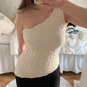 Vit oneshoulder topp  - Säljer en vit oneshoulder topp med snyggt strukturerat tyg. Toppen har en tight passform och är väldigt skön.