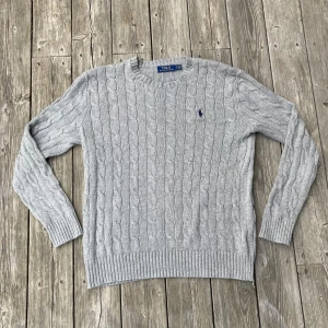Grå kabelstickad tröja från Polo Ralph Lauren - Grå kabelstickad Ralph Lauren tröja i mycket bra skick. Det finns inga defekter på tröjan och den är sparsamt använd. Storleken är S och den passar typ 172-178cm Hör av er om frågor!