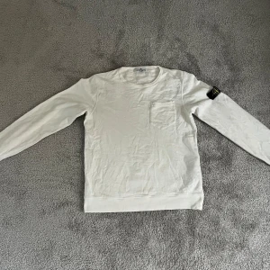 Vit långärmad tröja från Stone Island Junior - Säljer en stilren vit långärmad tröja från Stone Island Junior. Tröjan har en liten bröstficka och den klassiska Stone Island-loggan på ärmen. Priset kan såklart diskuteras, såklart äkta.