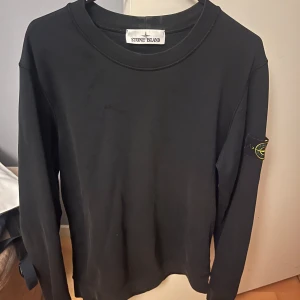 Svart långärmad tröja från Stone Island - Säljer en svart långärmad tröja från Stone Island med klassisk patch på ärmen. Tröjan har rund halsringning och är i ett mjukt material som passar perfekt till vardags. Enkel och stilren design.