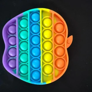 Regnbågsfärgad pop it i silikon - Säljer en pop it i form av ett äpple med regnbågsfärger. Gjord i mjukt silikon och perfekt för stresslindring eller som leksak. Färgerna går i lila, blå, grön, gul och orange. Enkel att ta med överallt.