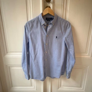 Polo Ralph Lauren skjorta - Hej, Säljer en stilren blå skjorta från Polo Ralph Lauren. Skjortan är i mycket bra skick utan några defekter och endast använd ett fåtal gånger. Skjortan är i slim fit och storlek S/18.