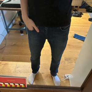 Mörkblå jeansbyxor herr - Säljer ett par klassiska mörkblå jeans med normal passform och raka ben. Jeansen har fem fickor och stängs med dragkedja och knapp. Perfekta för en stilren vardagslook.