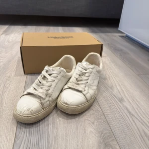 Vita sneakers från Zadig & Voltaire - Säljer ett par vita sneakers från Zadig & Voltaire med blixtdetalj på sidan. Skorna har snörning och är tillverkade i skinn. Klassisk rund tå och platt sula. Perfekta för dig som gillar stilrena och trendiga skor. Köpta för 2500, 2023. Inte använda på över ett år. Nya Sulor kan behövas köpa. Orginalförpackning och orginalskopåse är med. 